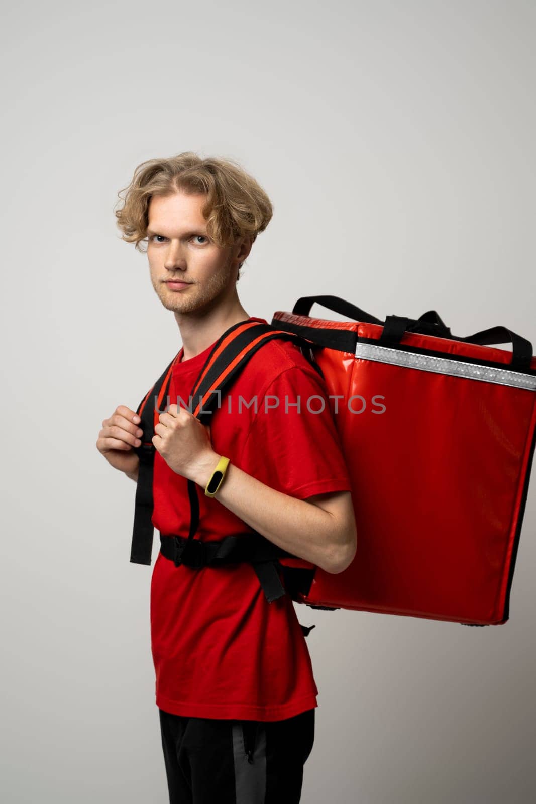 Side view of young courier in a red uniform and with a thermo bag on color red background, space for text. Fast express home delivery. Online order. by vovsht
