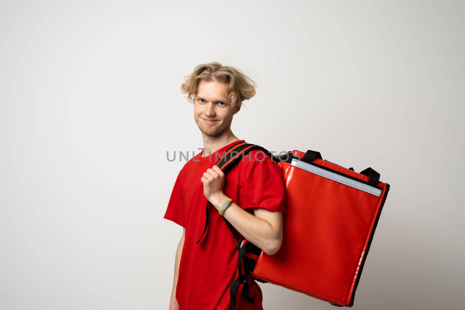 Courier delivers groceries home. Delivery man in red uniform with a thermal backpack isolated on a white background. Fast home delivery. Online order