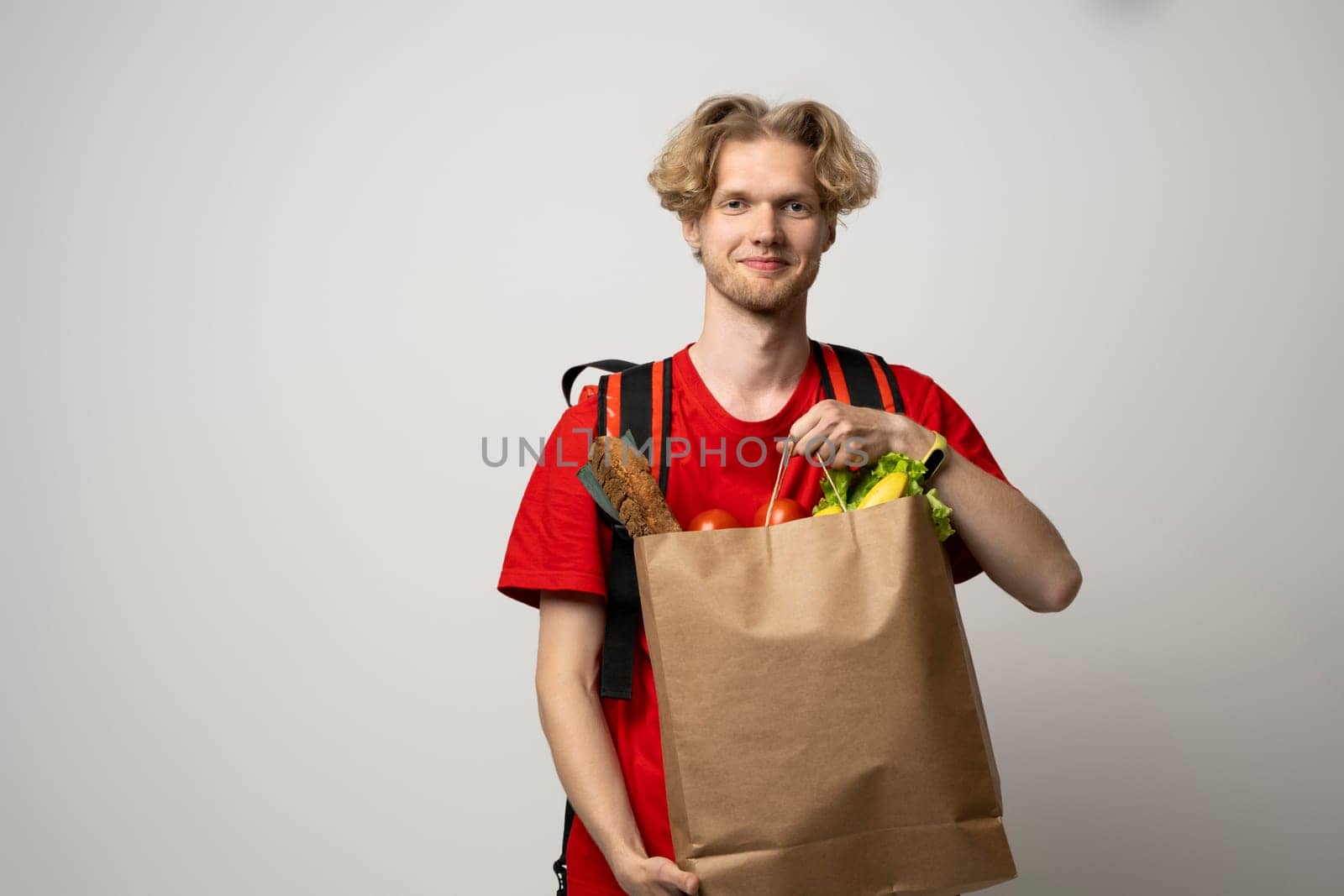 Delivery Concept. Handsome young delivery man in red uniform carrying package box of grocery food and drink from store, market on white studio background