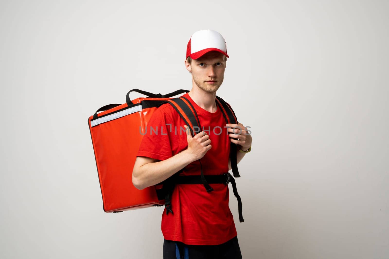 Young courier delivery man in red uniform with thermo backpack on white background. Fast express home delivery. Online order. by vovsht