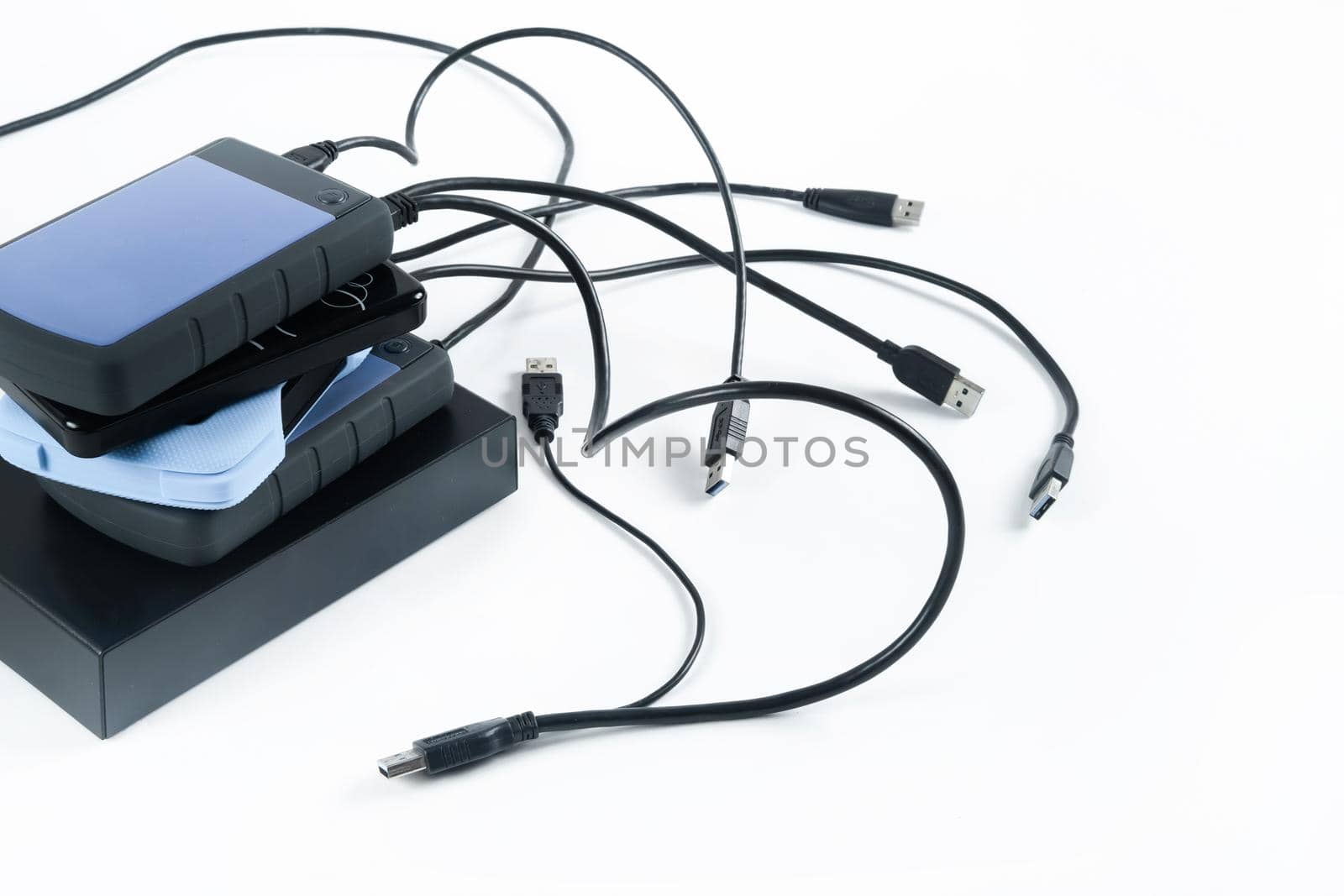 many external hard drives with wires lie on a white background. Hard drives on isolate. by Lobachad