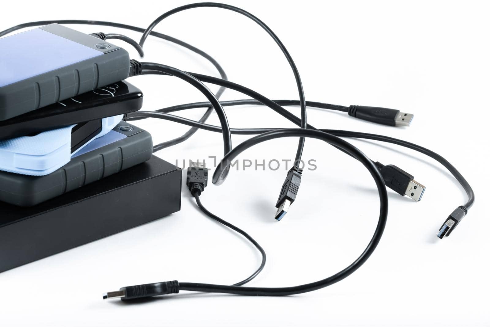 many external hard drives with wires lie on a white background. Hard drives on isolate. by Lobachad