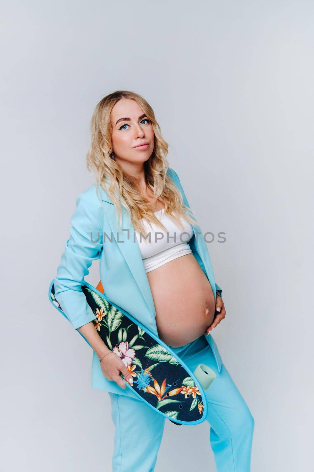 a pregnant girl in turquoise clothes with a skateboard in her hands on a gray background by Lobachad