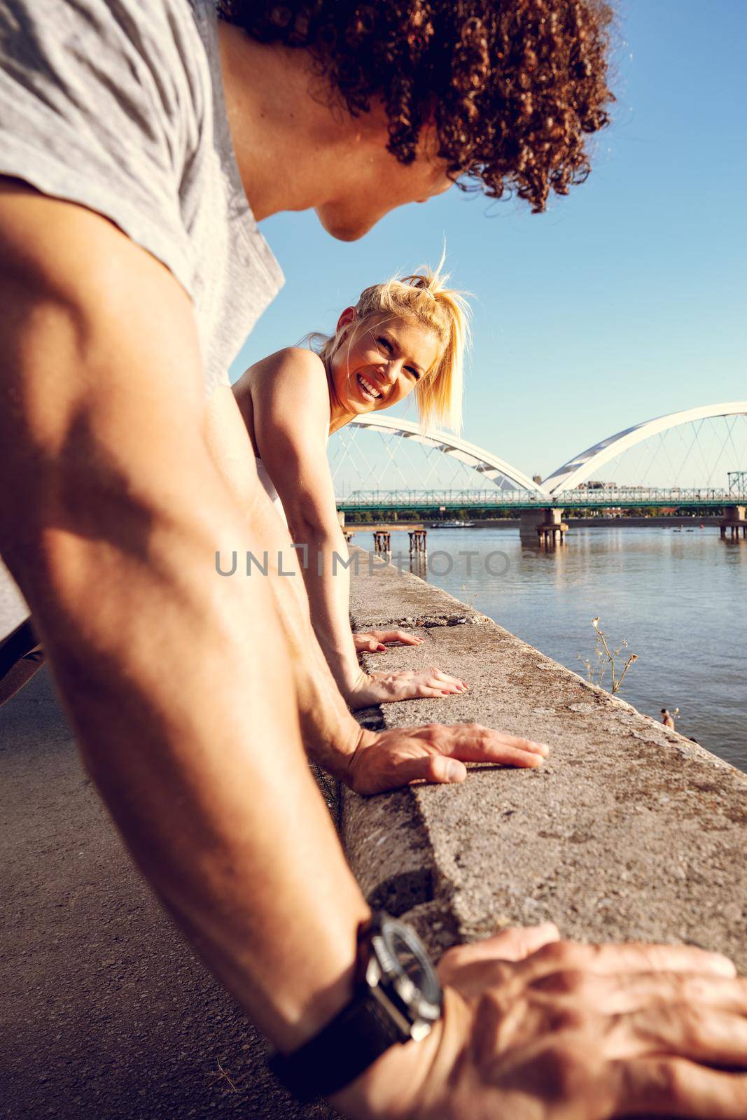 Young happy couple runners training outdoors doing push-ups during outdoor cross training by the river.