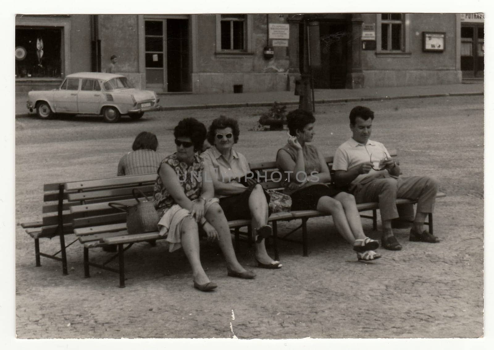 Retro photo shows a group of people sits on benches outdoor, 1960s. by roman_nerud