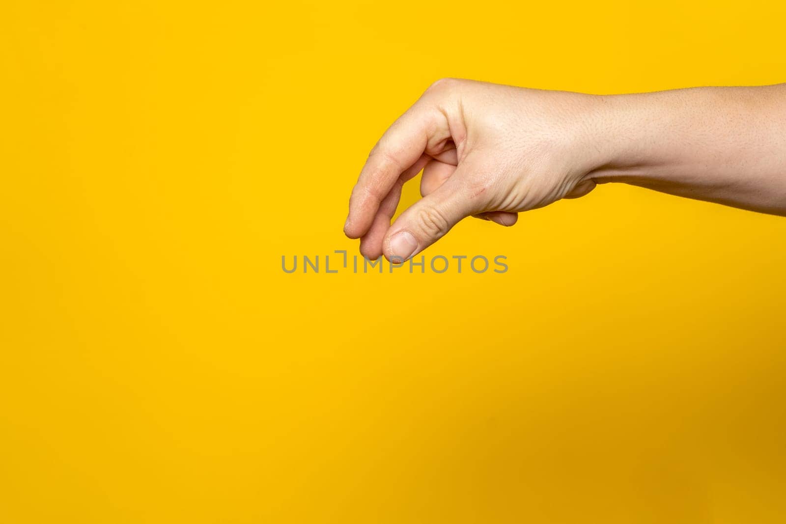 Tough man's hand making the gesture of picking up an object from above isolated on yellow background