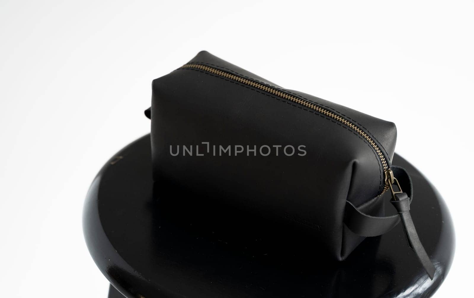 Side view black leather classic mens cosmetic bag with a metal gold zip on a black chair with a white background