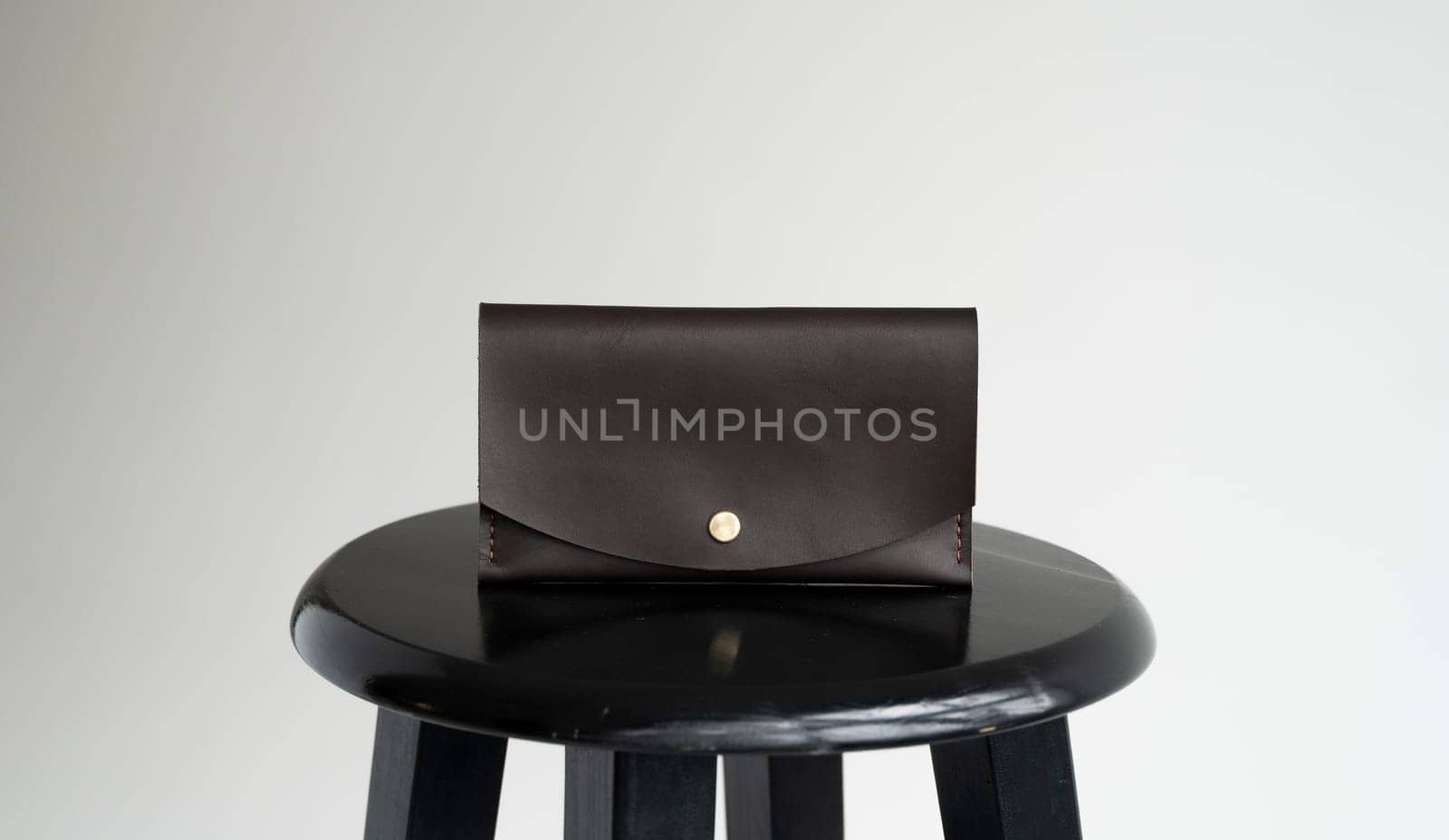 New brown genuine leather wallet on a wooden black chair with white background. Men's accessories
