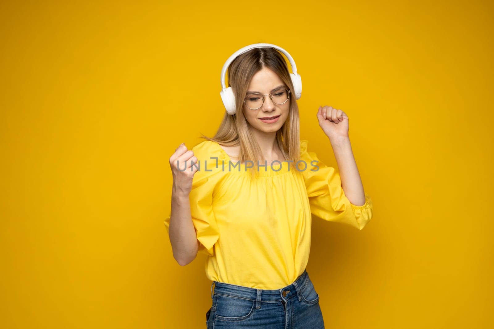 Lifestyle Concept. Portrait of beautiful woman in a glasses and yellow shirt joyful listening to music. Yellow studio background. Copy Space. by vovsht