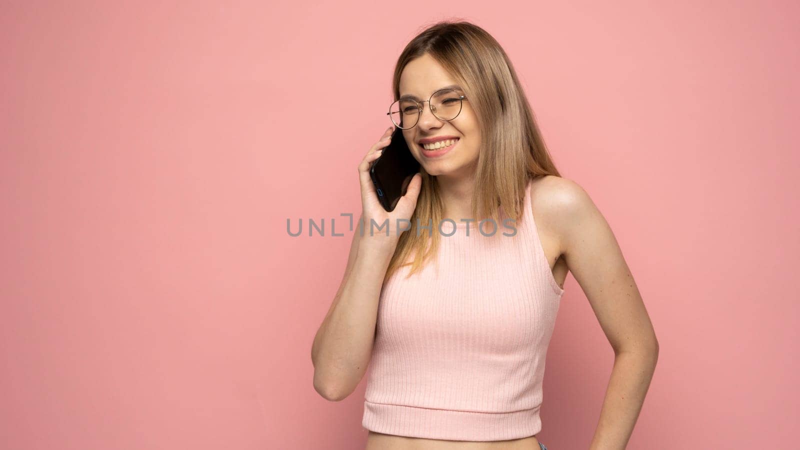 Portrait of beautiful girl wearing yellow shirt and holding mobile phone isolated over yellow background. by vovsht