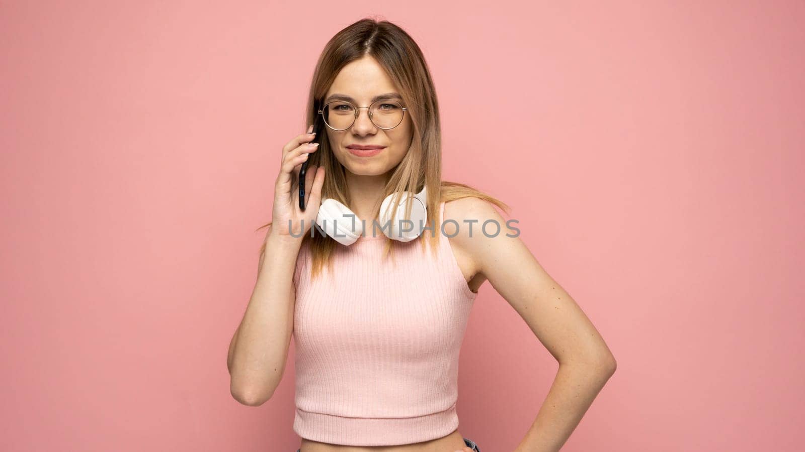 Portrait of a smiling girl dressed in yellow shirt and glasses talking on mobile phone and looking at camera isolated over yellow background