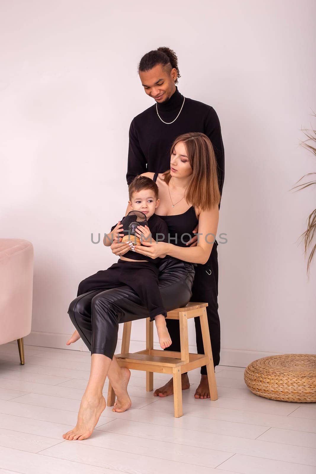 A stylish multi-racial family in black clothes, sitting in light room by Zakharova