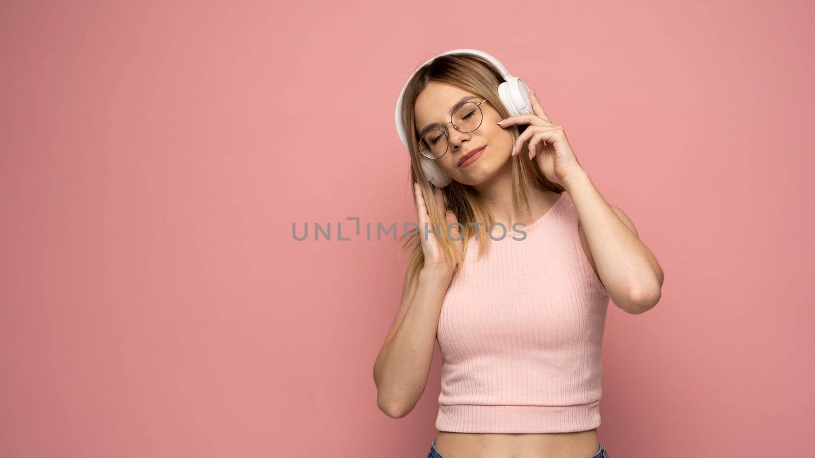 Lifestyle Concept. Portrait of beautiful woman in a glasses and pink shirt joyful listening to music. Pink studio background. Copy Space