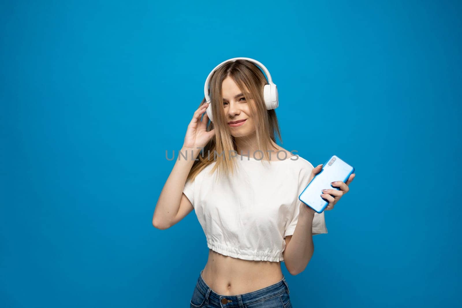 Smiling caucasian blonde young woman listening to the podcast, e-book or music in headphones isolated on blue background. by vovsht