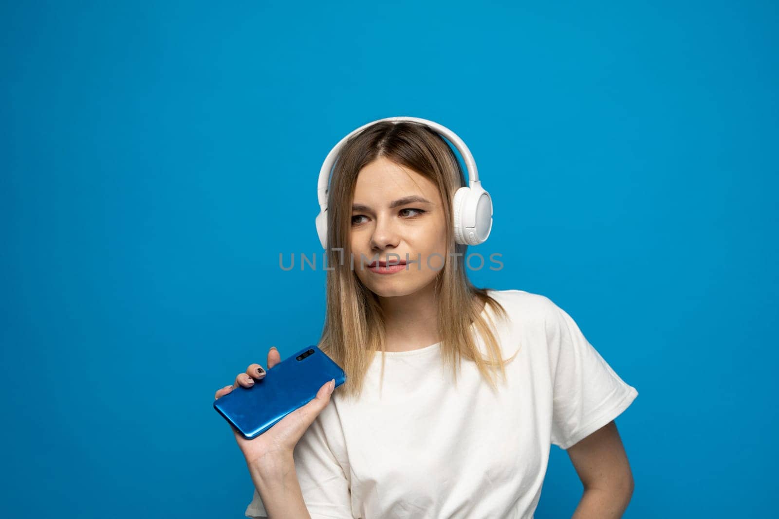 Happy young blonde woman in a white t-shirt dancing to the music she is listening to on her phone. by vovsht