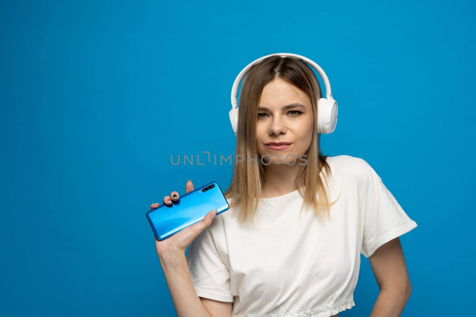 Beautiful young blonde woman with headphones and mobile device listening to music and smiling and dancing, isolated on blue background. by vovsht