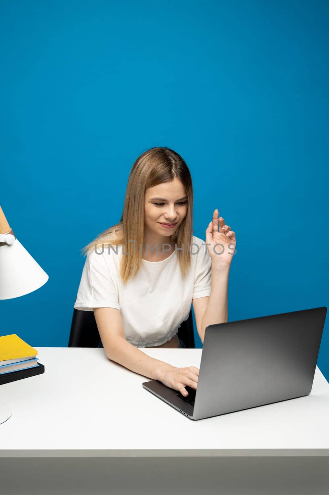Hello there. Pleasant young female freelancer sitting at studio before laptop screen waving hand to web camera. Student starting distant lesson, lecture or training course online. by vovsht
