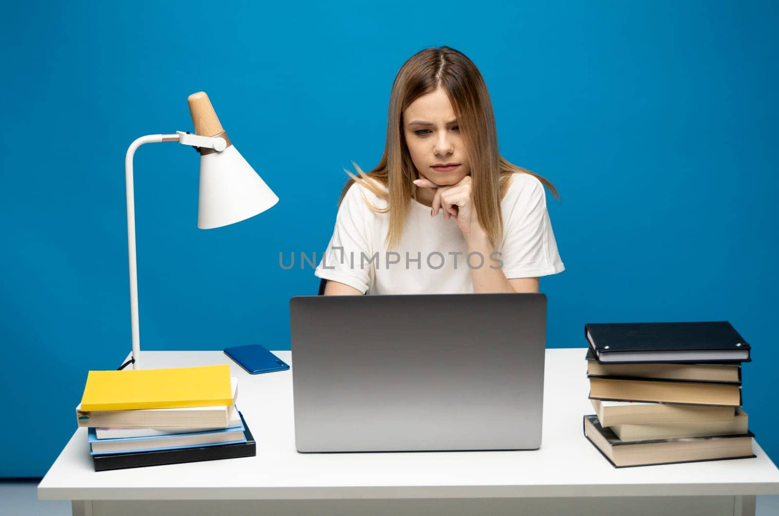 Studio portrait of young successful secretary employee business woman wear white t-shirt sit work at white office desk with laptop browsing internet online isolated on blue background. by vovsht