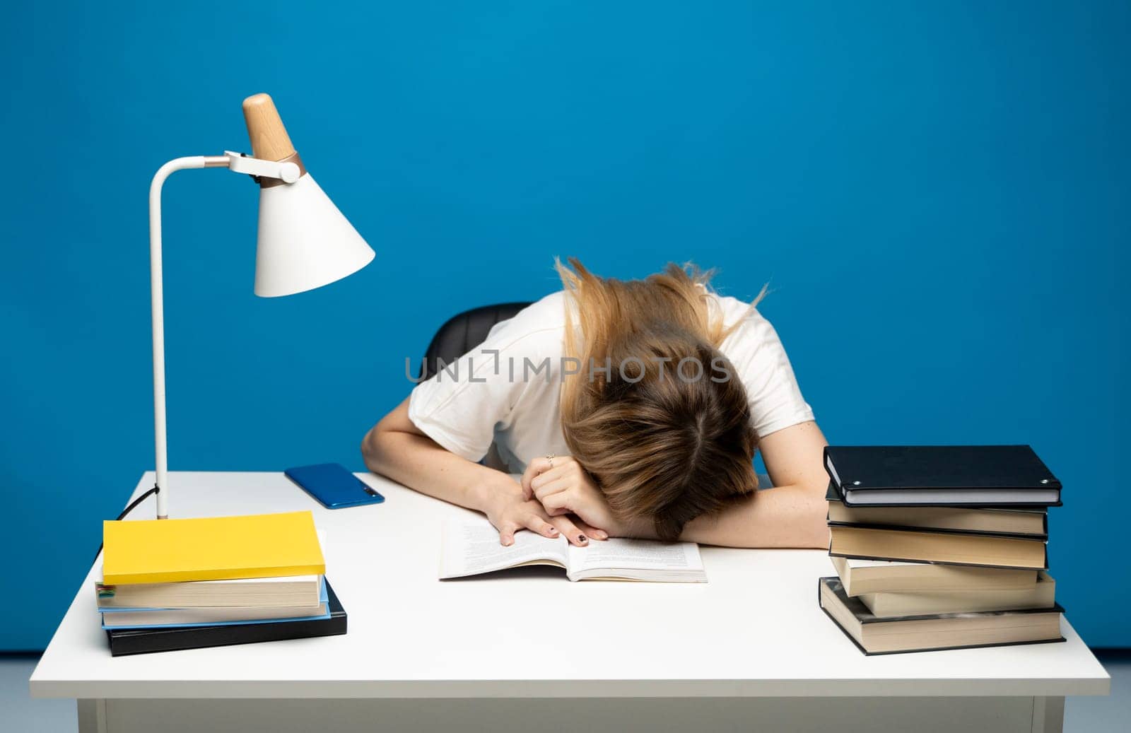 Tired student girl with glasses sleeping on the books in the library. Student studying hard exam and sleeping on books on a blue background