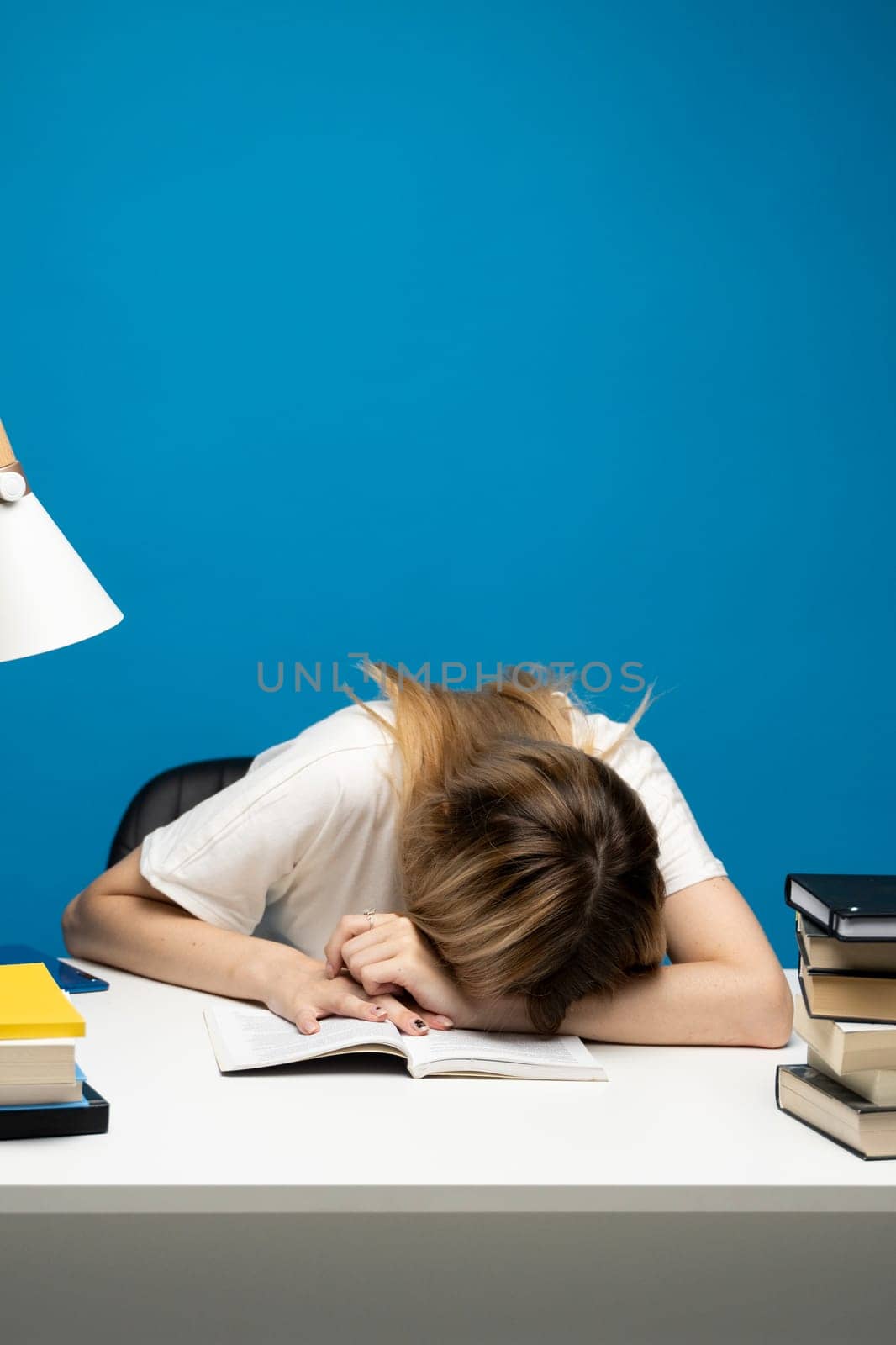 Student studying exam and sleeping on books on a blue background. Tired student girl with glasses sleeping on the books in the library. by vovsht