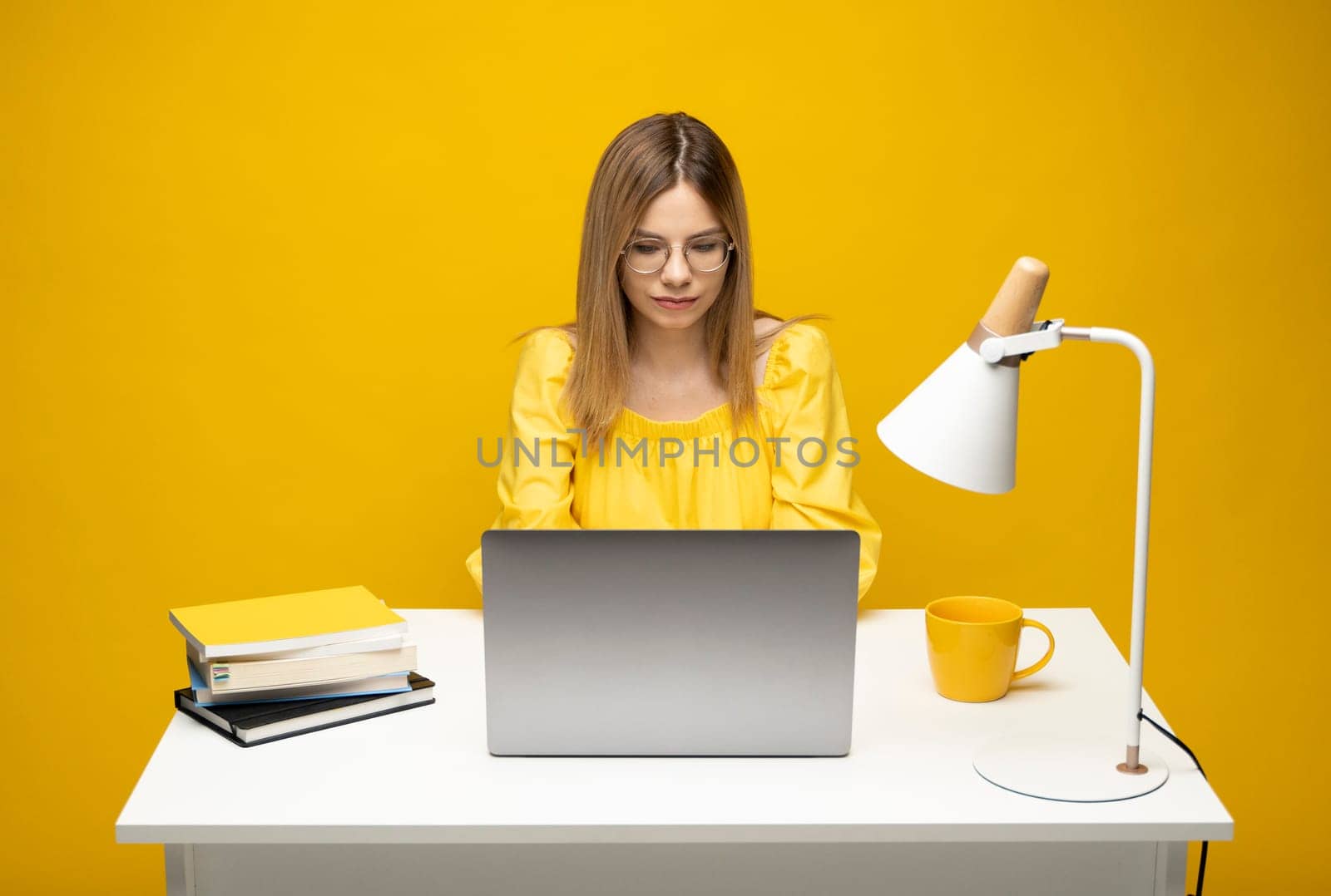 Smiling millennial girl student sit at desk watching educational webinar or online course on laptop. Happy young woman use computer gadget working distant from home. by vovsht