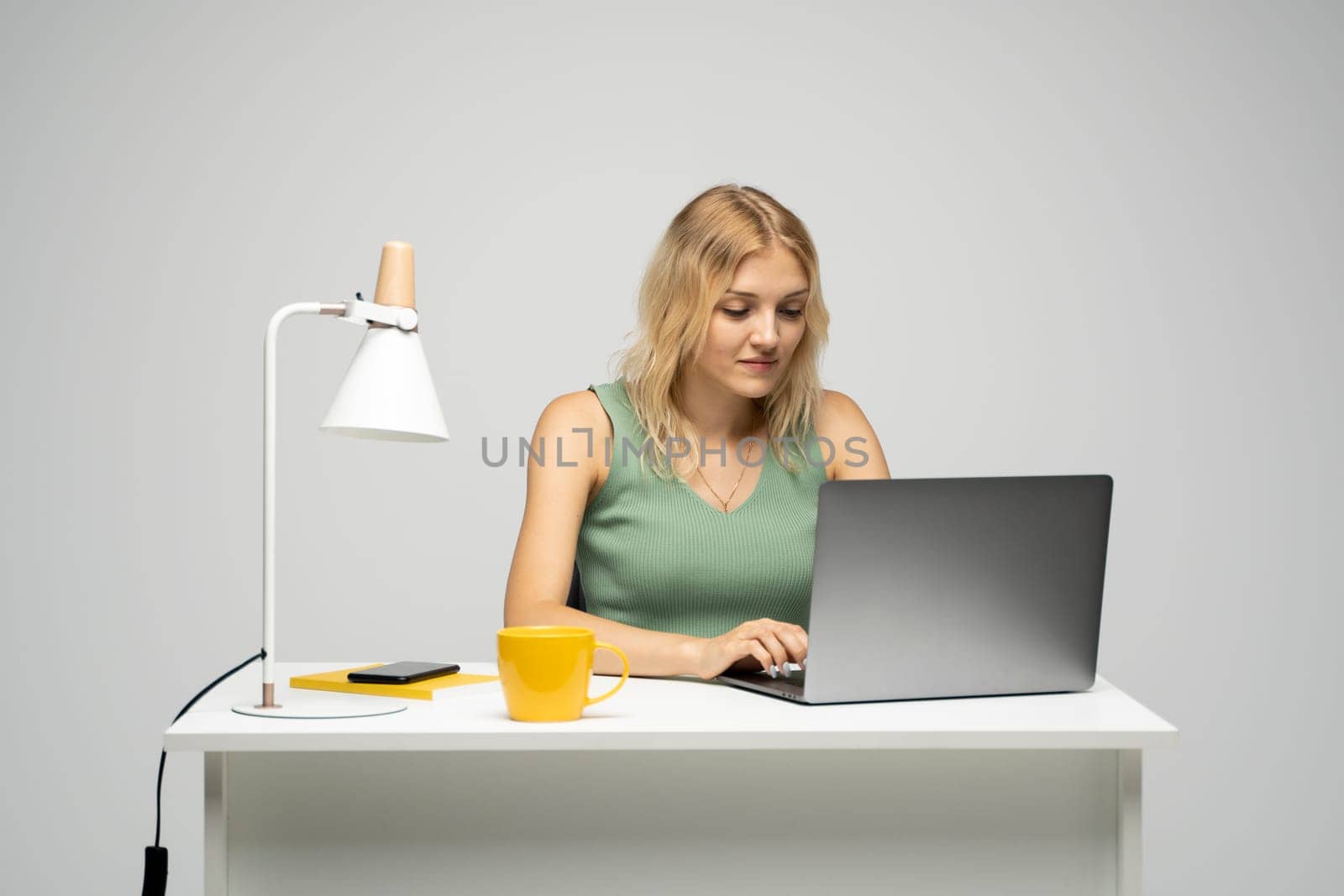 Portrait of a pretty young woman studying while sitting at the table with grey laptop computer, notebook