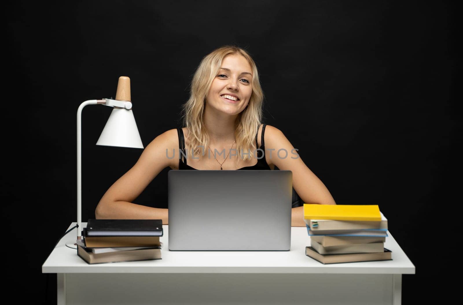 Excited young woman working with a grey laptop computer, notebook while sitting at the table. Smiling business woman or student received a good news isolated on a black background