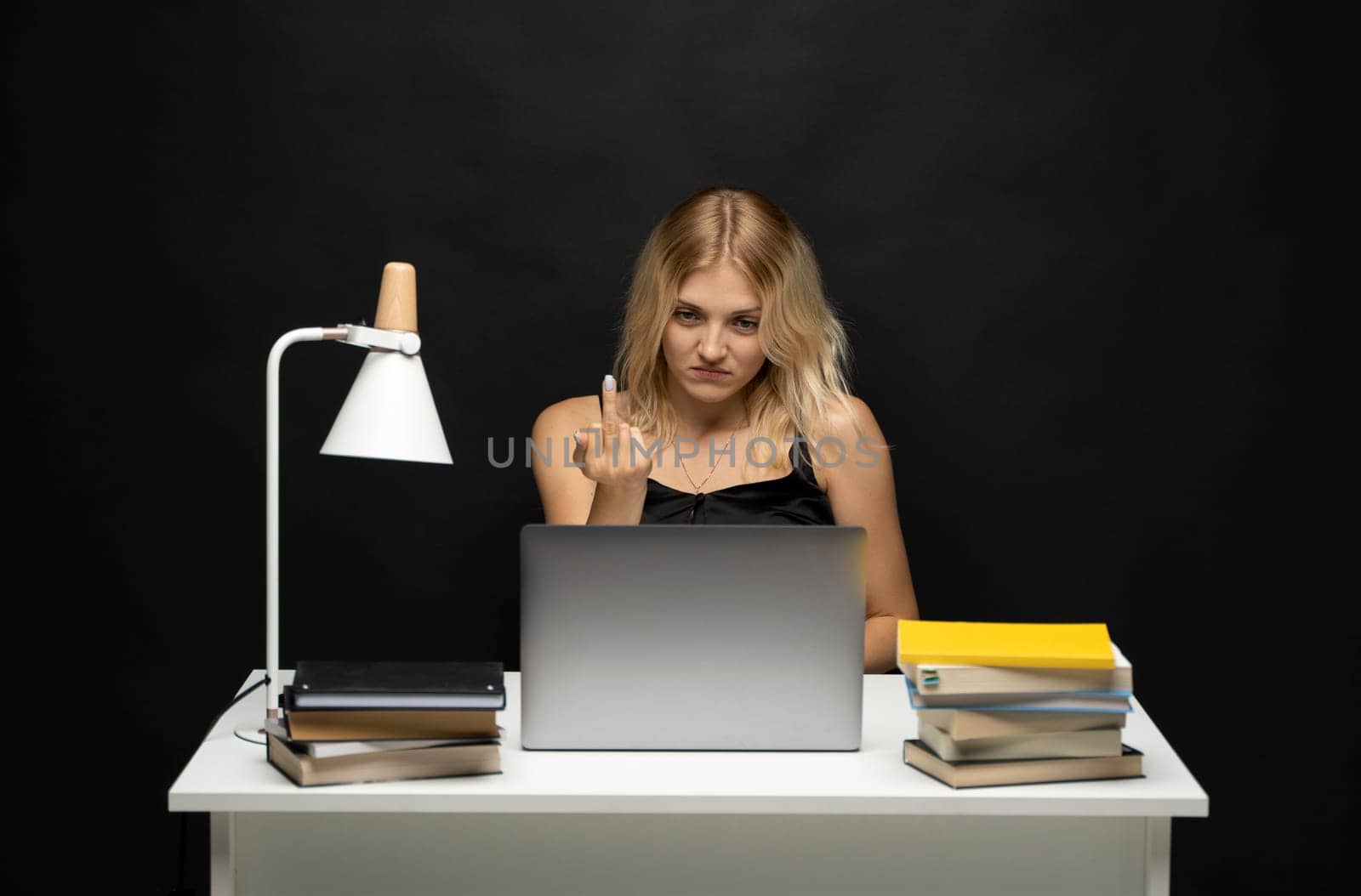 Portrait of young woman sitting at the table and showing middle finger in a laptop. by vovsht
