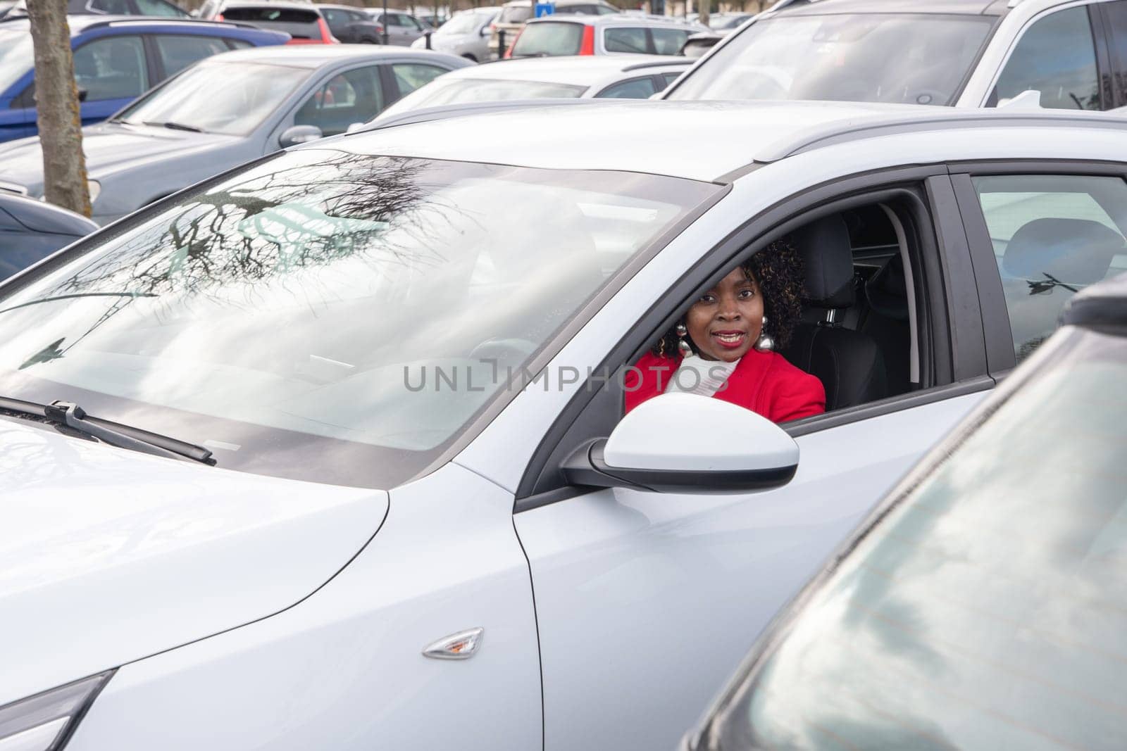 African american woman in red coat driving with a white car out of the parking lot, personal transport, high quality photo