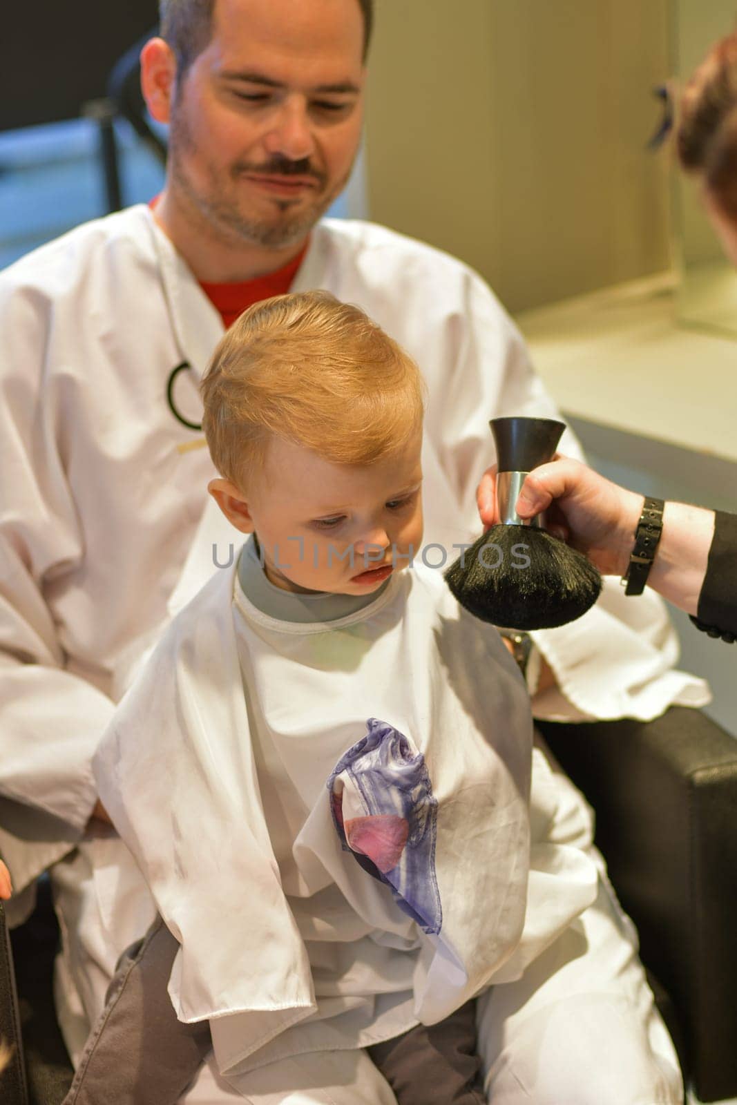 Dad holds a little boy of a one years old at the hairdresser for a first haircut