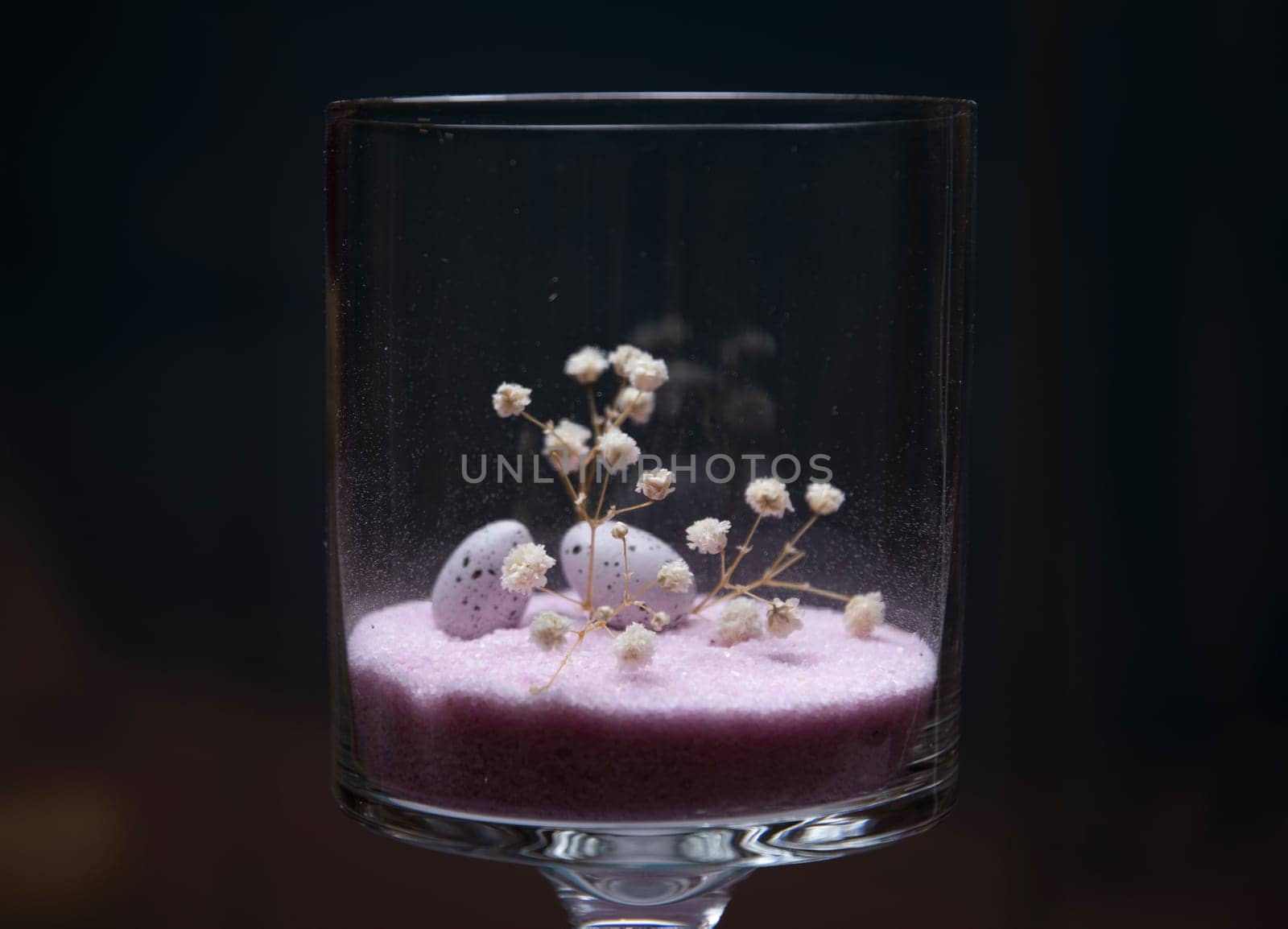 A glass with Easter eggs on pink sand background, holiday decoration. High quality photo