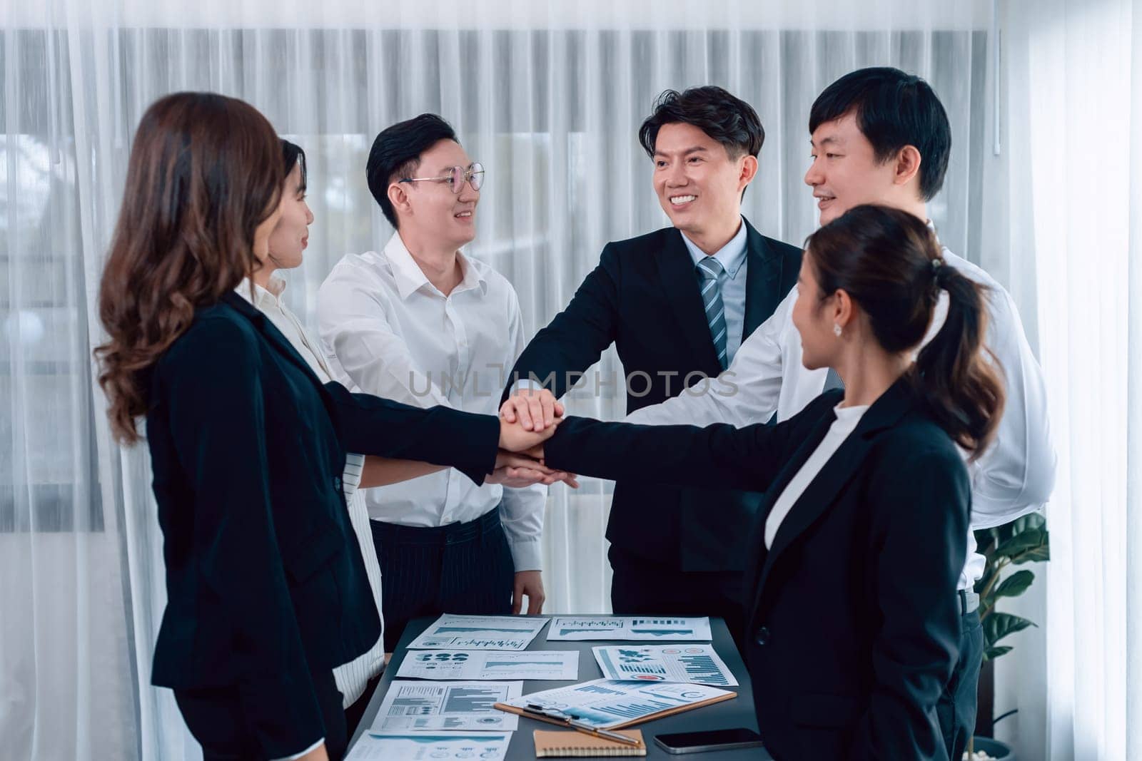 Closeup business team of suit-clad businessmen and women join hand stack together and form circle. Colleague collaborate and work together to promote harmony and teamwork concept in office workplace.