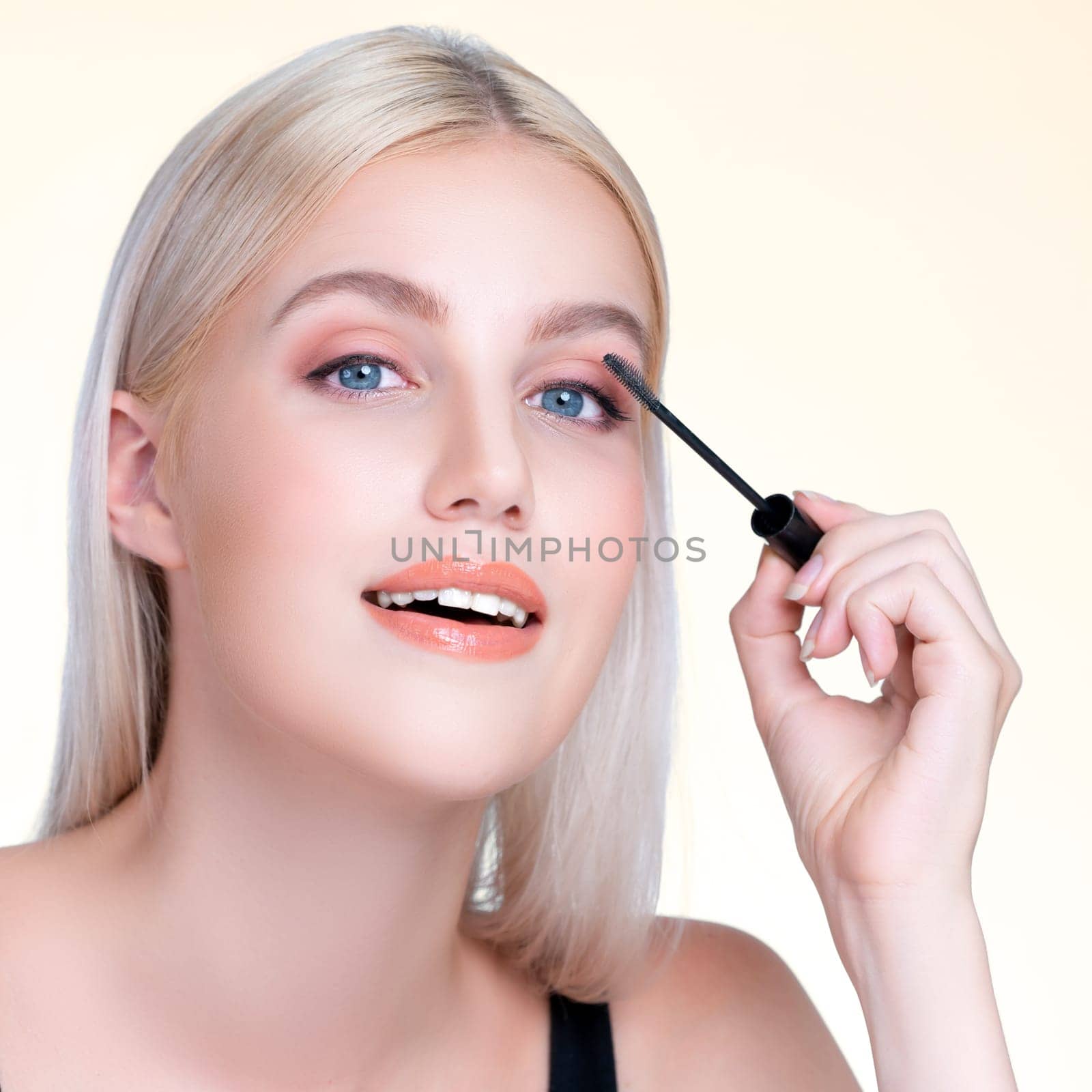 Closeup personable woman with blond hair putting black mascara with brush in hand on long thick eyelash. Perfect fashionable cosmetic clean facial skin with beautiful eye young woman.