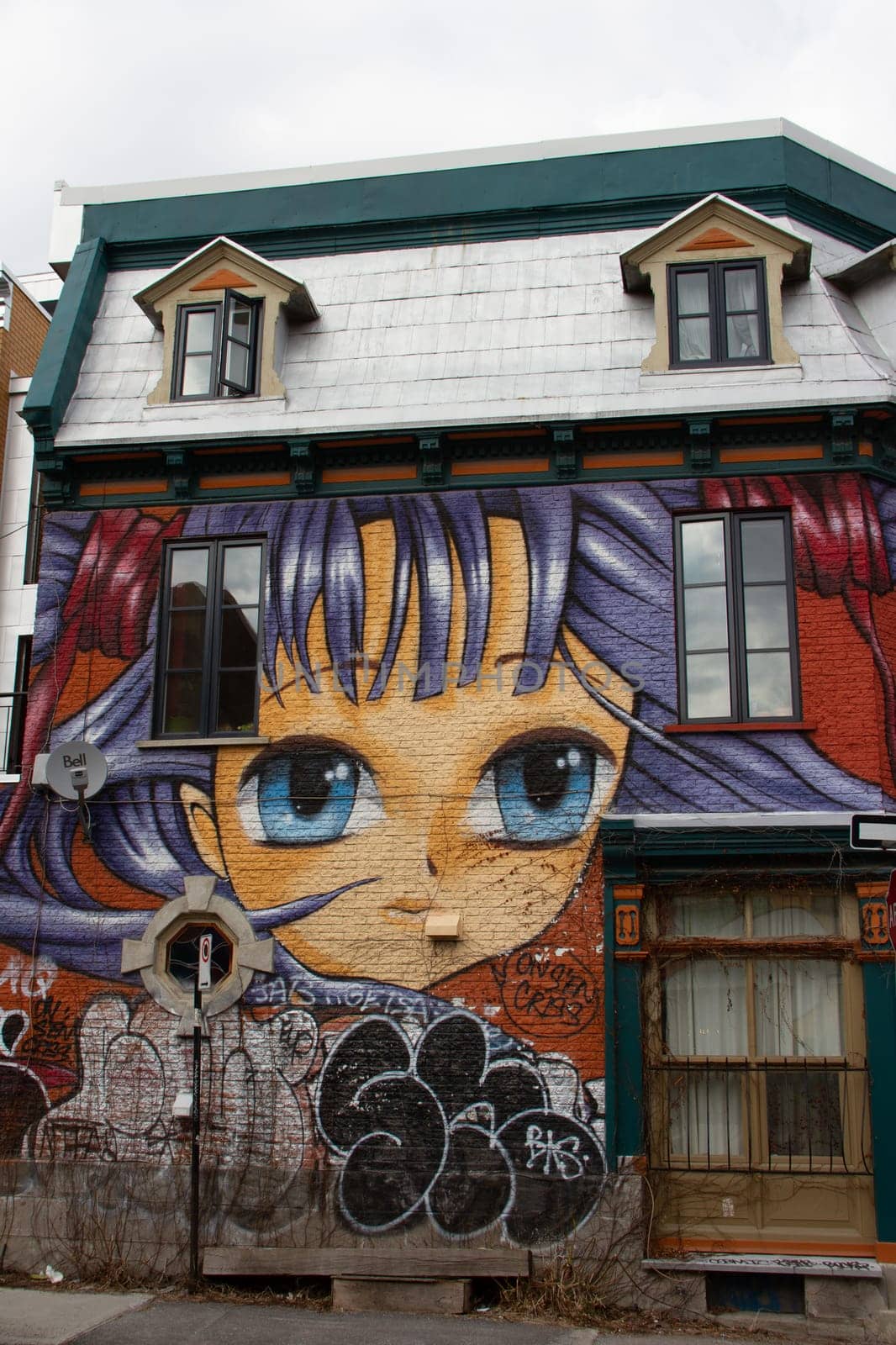 Creative graffiti street art mural lining a house of Montreal, Quebec, Canada. A house with a painting of a girl with purple hair and blue eyes.
