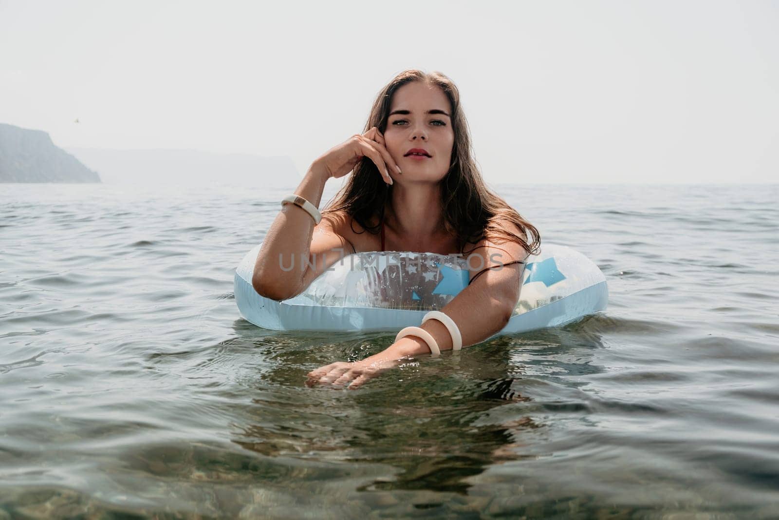 Woman summer sea. Happy woman swimming with inflatable donut on the beach in summer sunny day, surrounded by volcanic mountains. Summer vacation concept