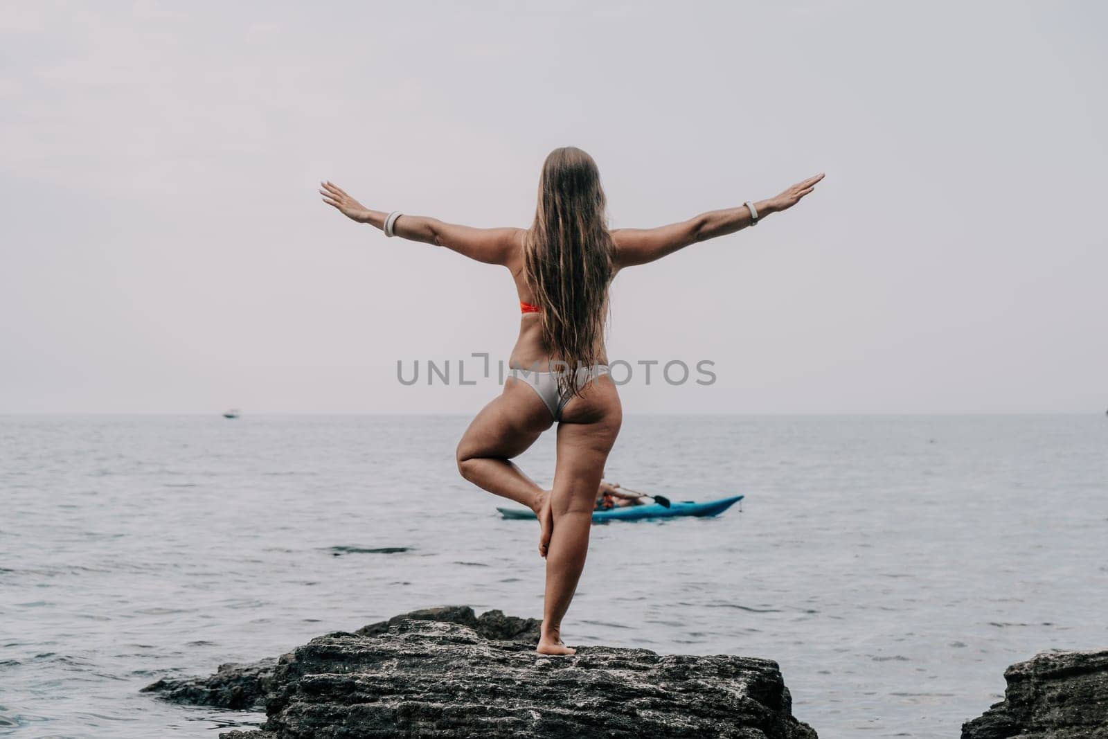 Woman meditating in yoga pose silhouette at the ocean, beach and rock mountains. Motivation and inspirational fit and exercising. Healthy lifestyle outdoors in nature, fitness concept.