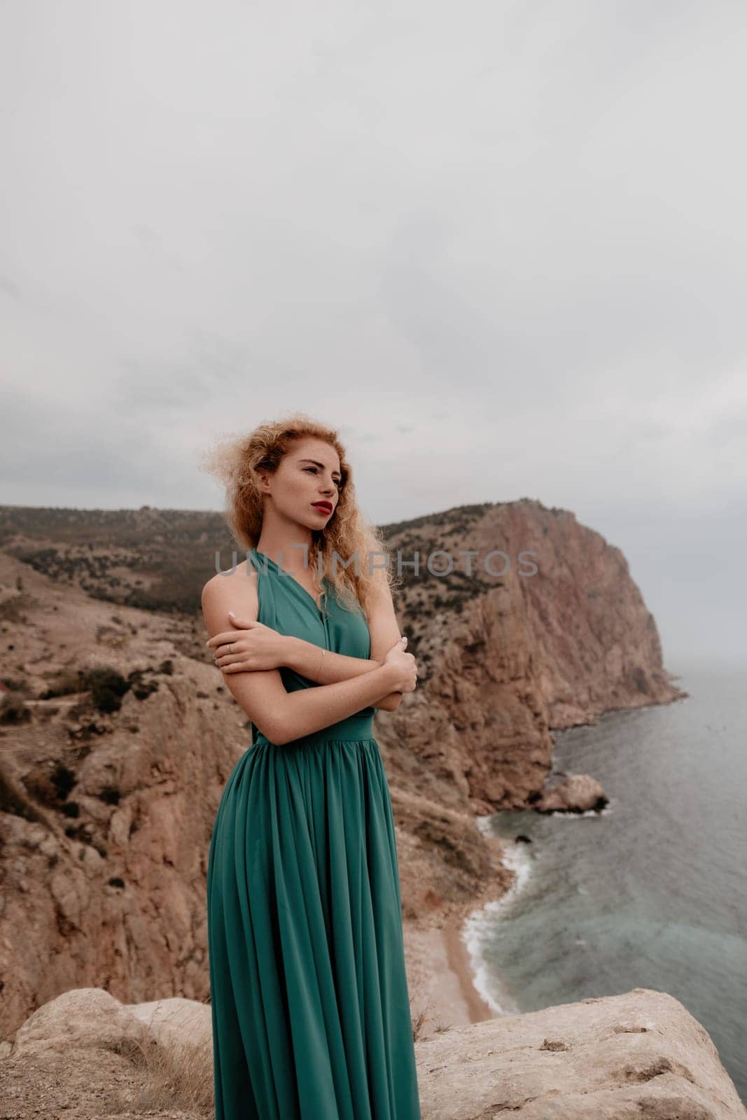 Side view a Young beautiful sensual woman in a mint long dress posing on a volcanic rock high above the sea during sunset. Girl on the nature on overcast sky background. Fashion photo