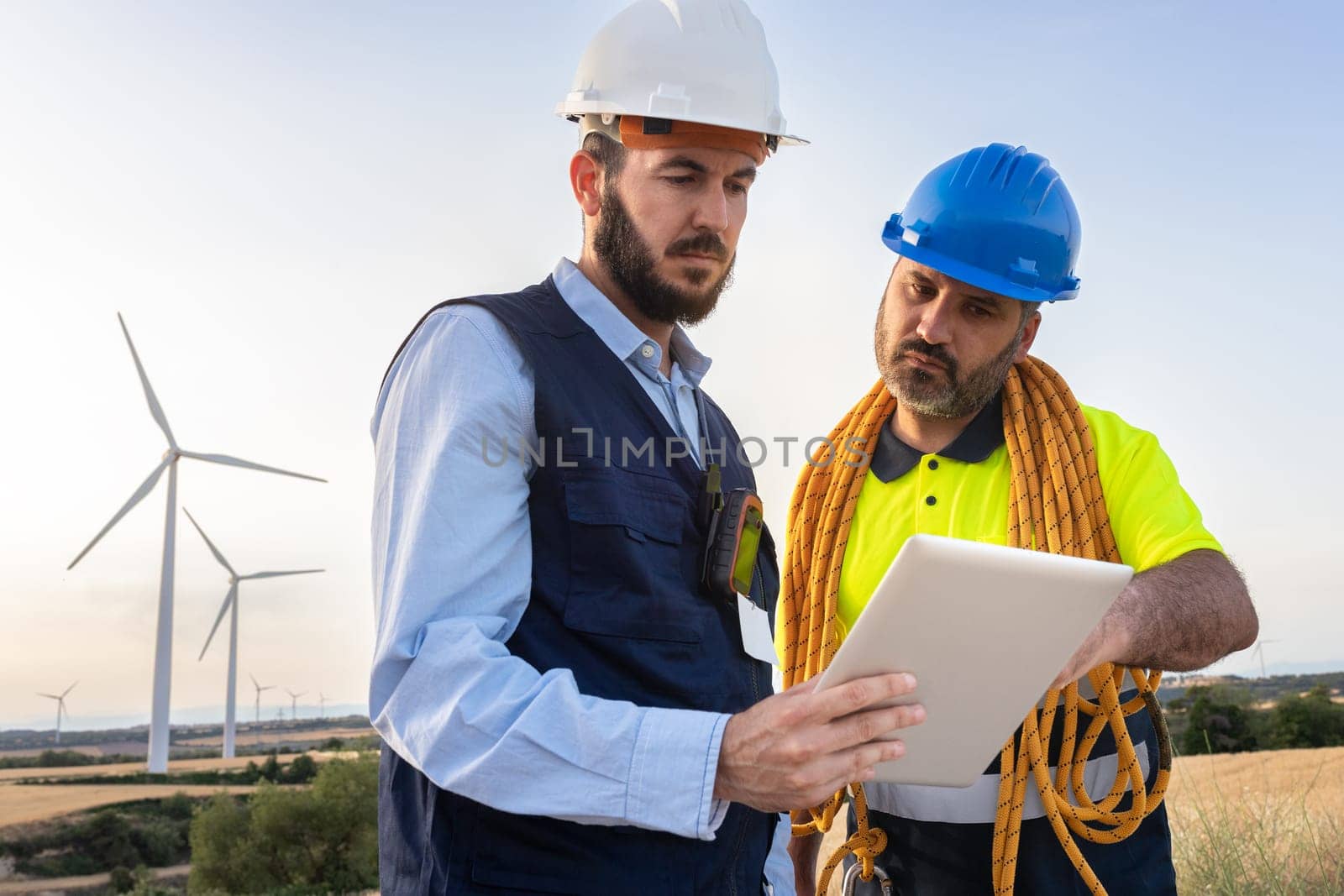 Engineer and wind turbine farm maintenance worker looking together plans in digital tablet. Renewable energies concept.