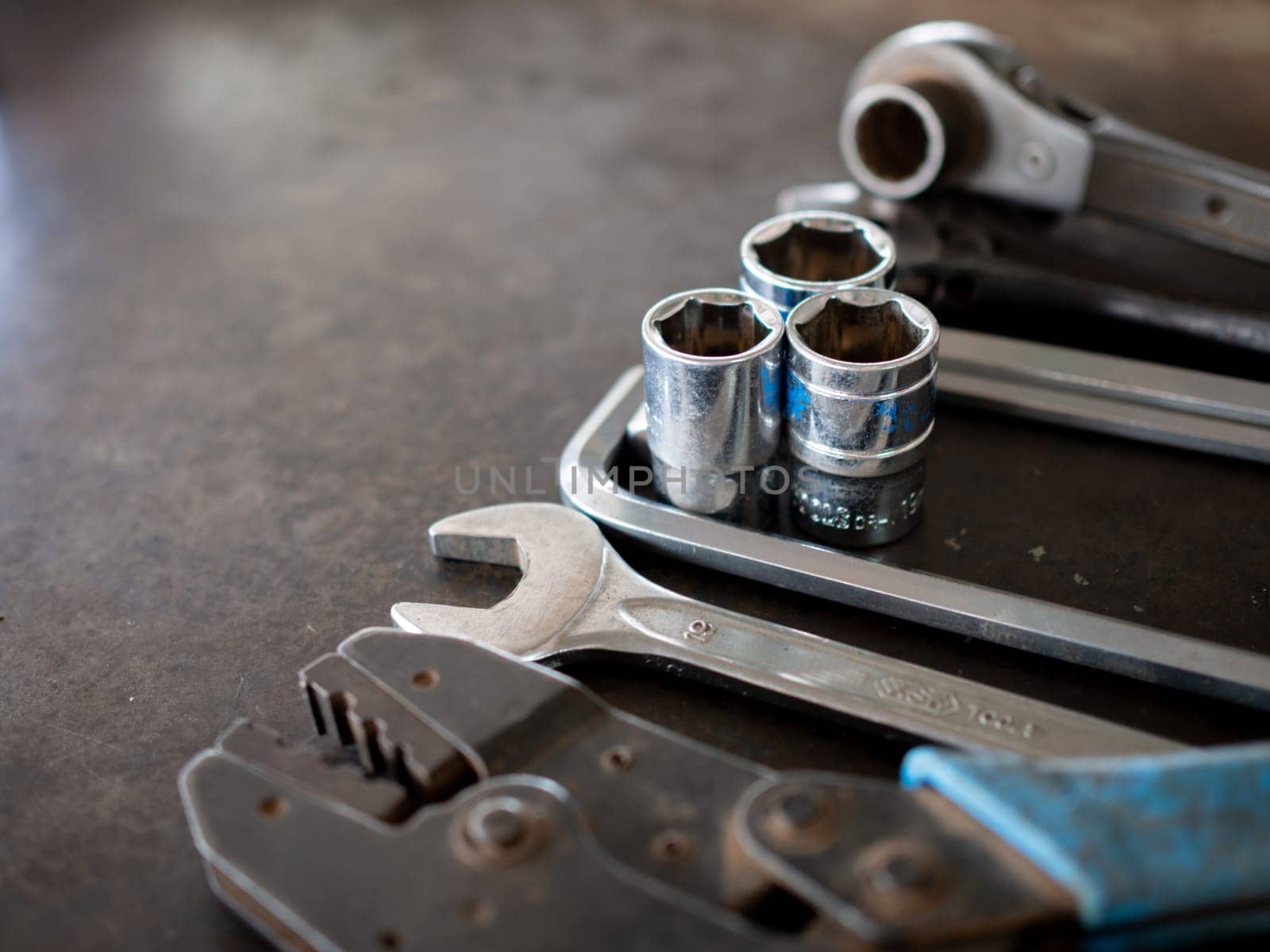 Hand tools consisting of wrenches, pliers, socket wrenches, laid out on old steel plate background.