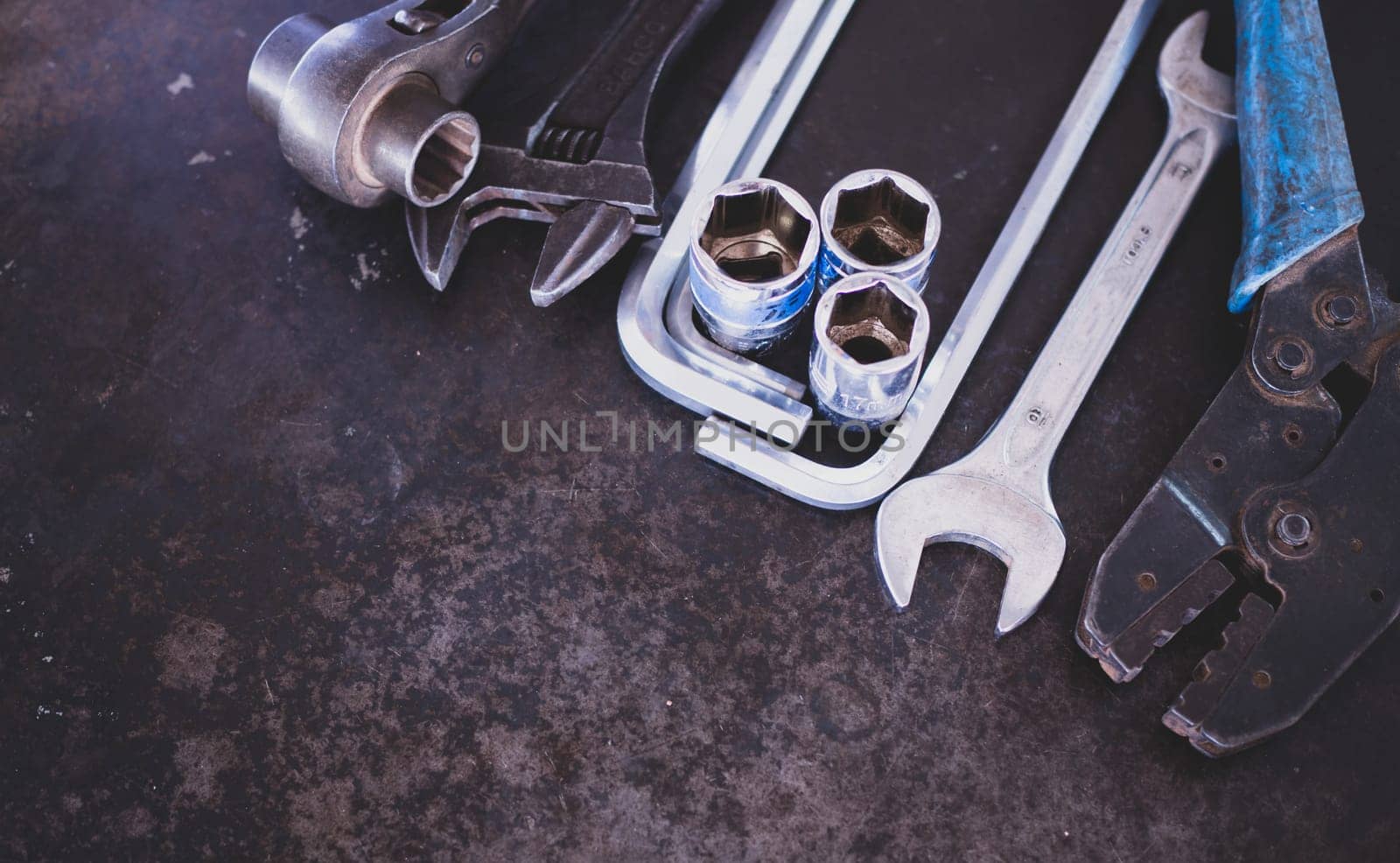 Hand tools consisting of wrenches, pliers, socket wrenches, laid out on old steel plate background.