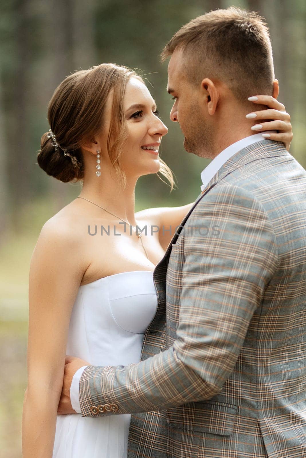 young couple bride in a white short dress and groom in a gray suit in a pine forest among the trees