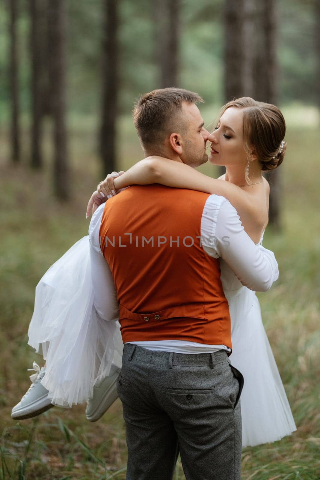 young couple bride in a white short dress and groom in a gray suit in a pine forest among the trees