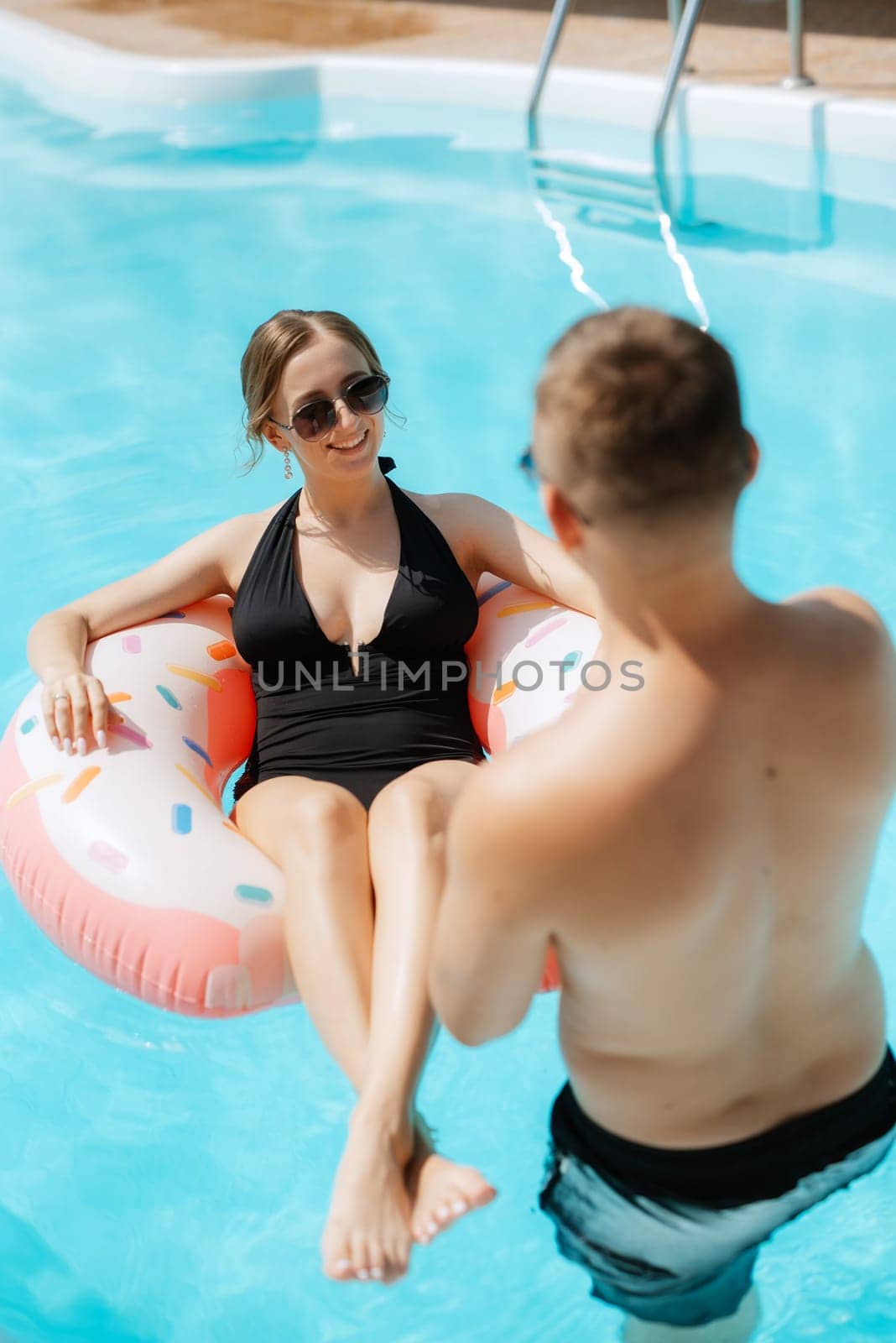 guy and a girl in bathing suits are relaxing, near the blue pool by Andreua