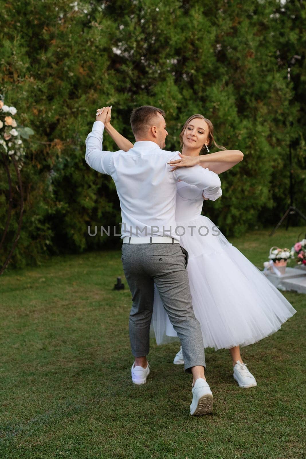 the first dance of the groom and bride in a short wedding dress on a green meadow