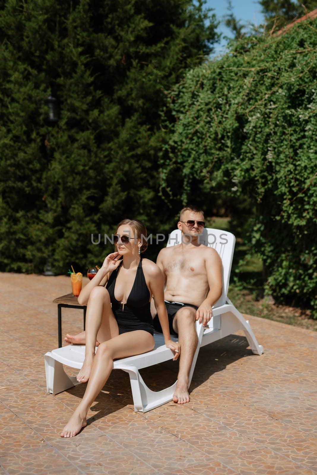 guy and a girl in bathing suits are relaxing, near the blue pool by Andreua