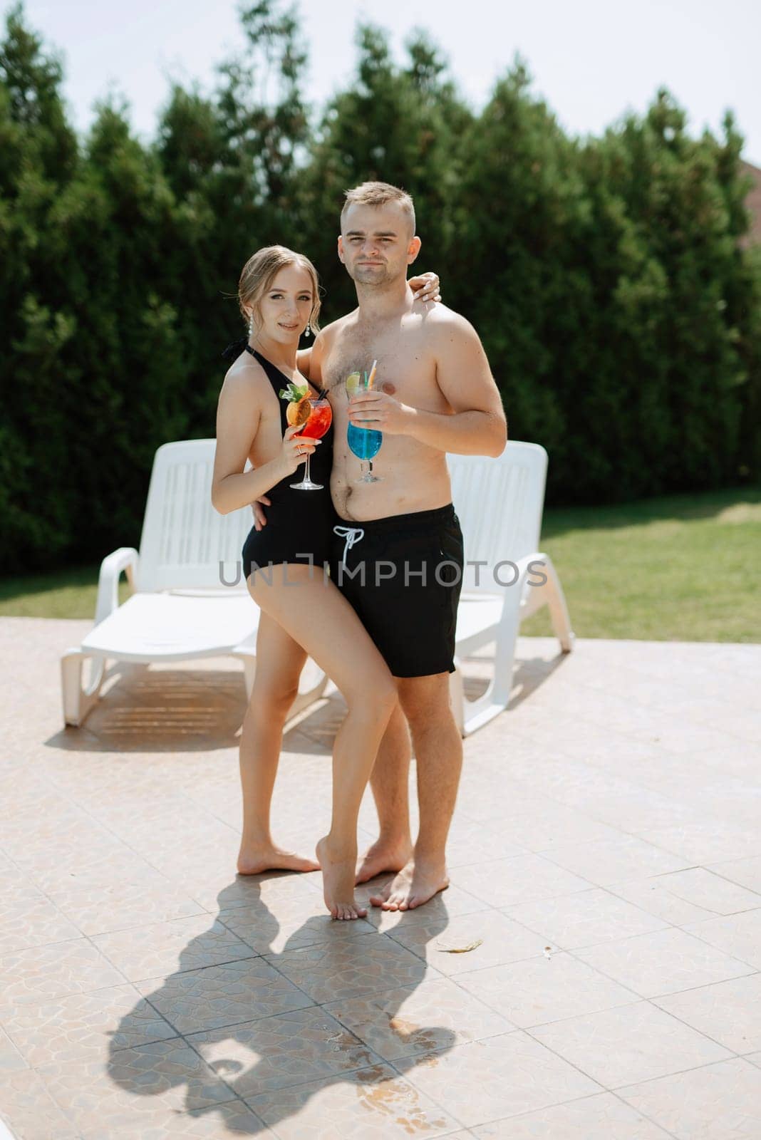 guy and a girl in bathing suits are relaxing, near the blue pool by Andreua