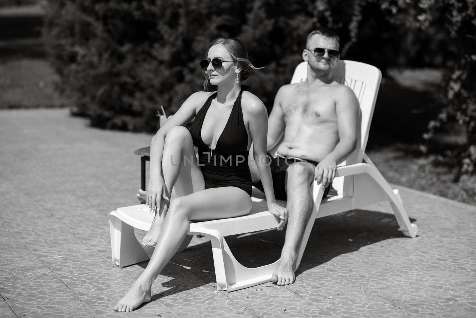 guy and a girl in bathing suits are relaxing, near the blue pool by Andreua