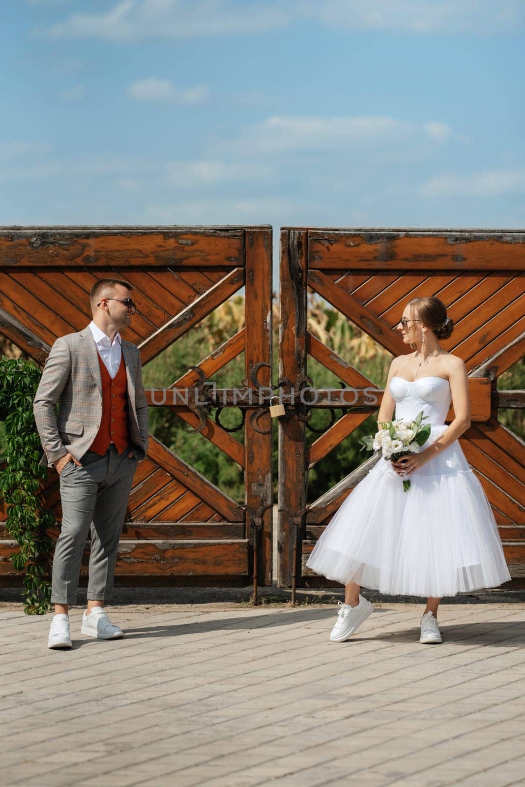 young couple bride in a white short dress and groom in a gray suit near the wooden gate by Andreua