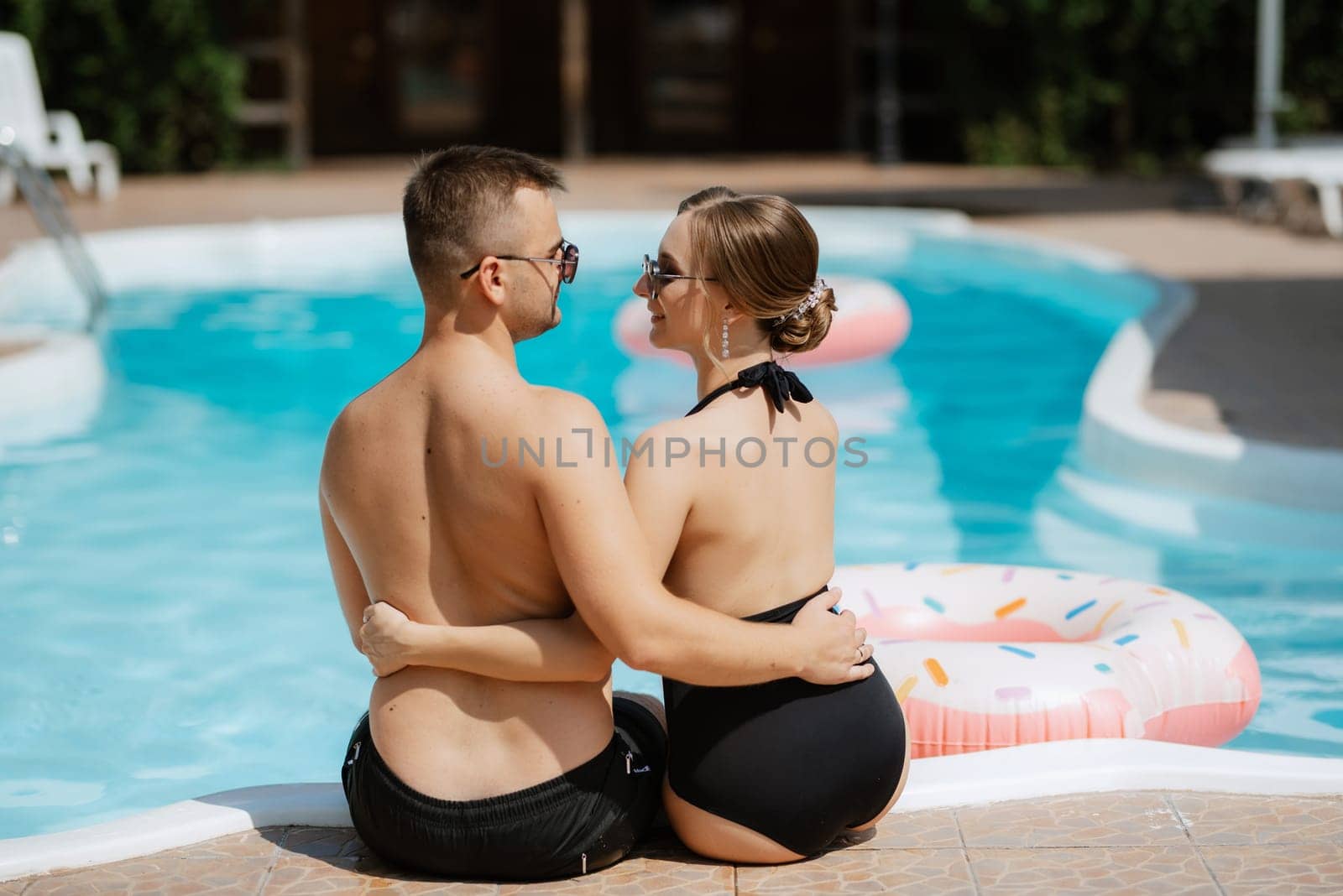 guy and a girl in bathing suits are relaxing, near the blue pool by Andreua