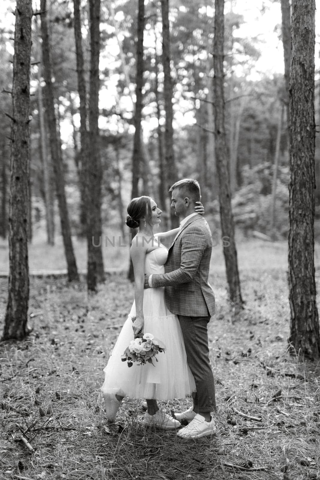 young couple bride in a white short dress and groom in a gray suit in a pine forest among the trees